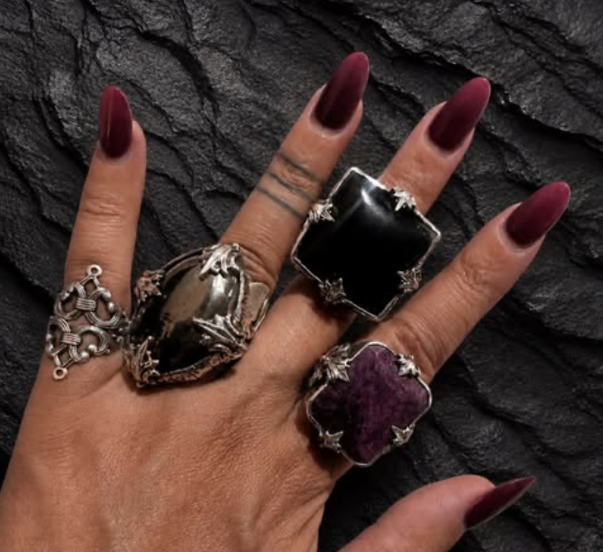 Close-up of a hand wearing statement silver rings with black, purple, and smoky gemstones.
